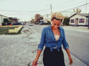 Brit in a denim shirt tied at the waste, smiling and looking down at the ground