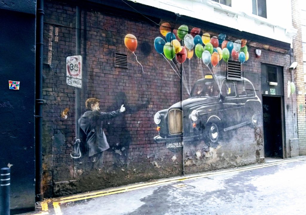 Glasgow street art, man hails taxi with balloons tied to it