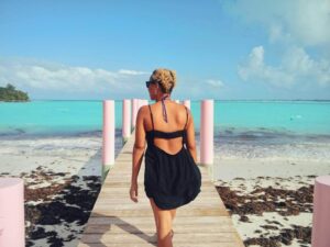 Brit's back in a black backless sun dress at the treasure cay public dock. The beach is flanking the dock and crystal blue water is in the background.