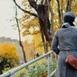 woman in a coat walking alone uphill with back to camera and hands in her pocket