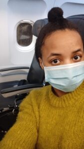 Woman in a green jumper sitting on plane with a disposable mask on, Flying, covid and my autoimmune disease