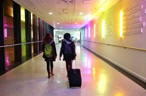 The rear view of two women walking side by side through an empty airport corridor