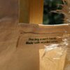 A close up of the inner tag of the tote bag which states, " This bag is earth friendly >> Made with recycled cotton." There is pampas grass on the side of the label